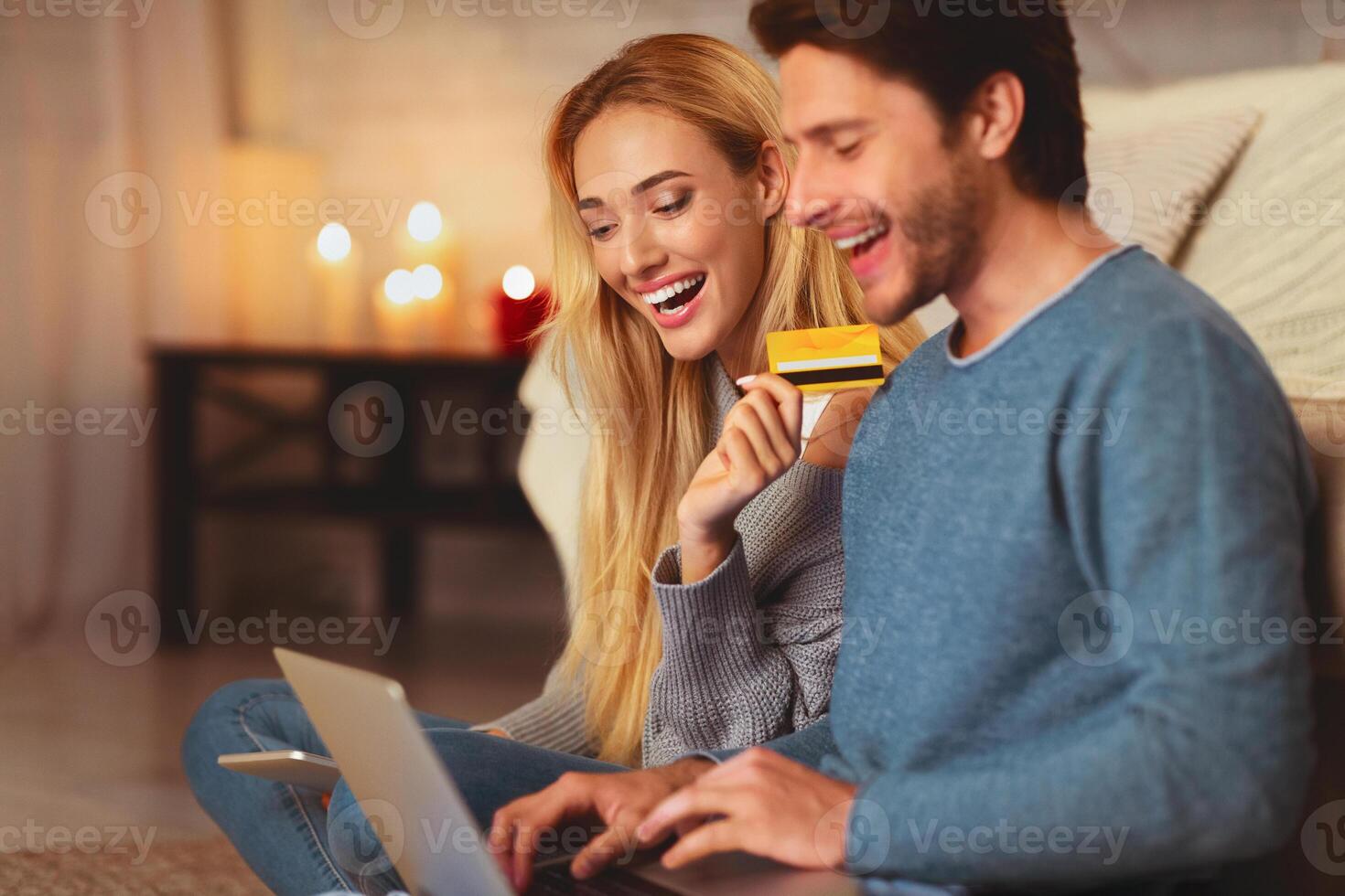 Cheerful Couple Making Online Order Using Laptop Computer And Credit Card Sitting On Floor Indoor. Selective Focus photo