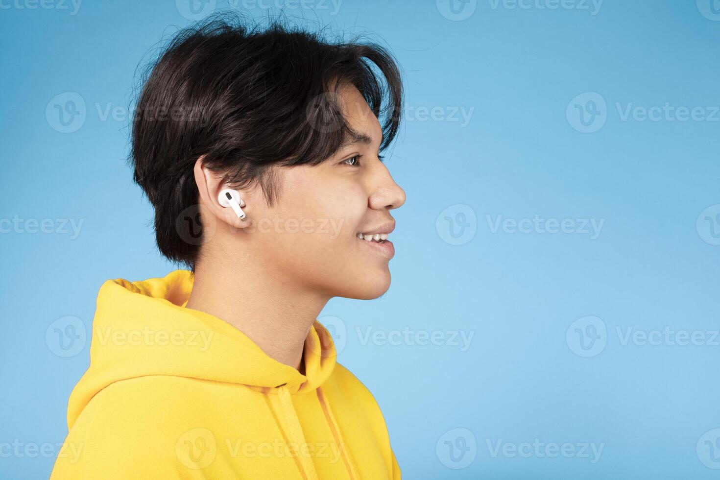 Asian young guy is shown wearing ear buds on his ears, immersed in listening to music. He appears focused on the music playing through the ear buds, copy space photo