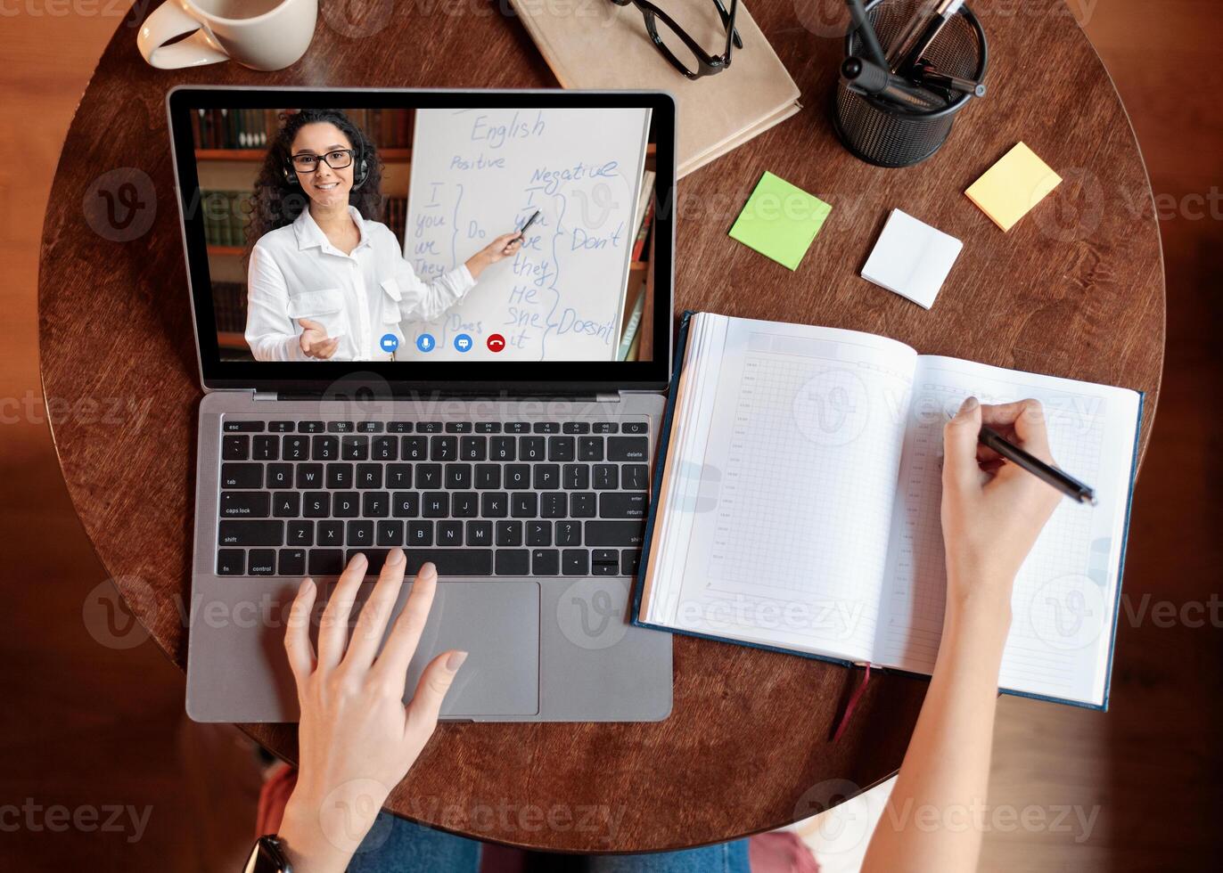 Distance Education Concept. Above top view of female student sitting at desk, writing in notebook, taking notes, using laptop, having online class with teacher. Remote studying from home, quarantine photo