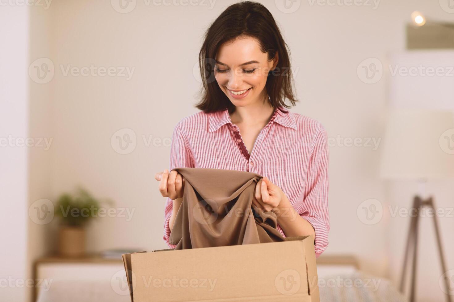 Moving Concept. Excited girl getting ready for moving out, packing clothes in paper box, copyspace photo