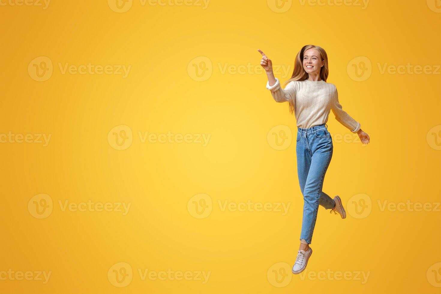 Look there. Cheerful teen girl jumping and pointing aside on copy space over orange background photo