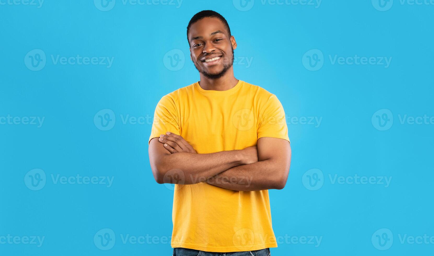 Cheerful African American Guy Smiling To Camera Posing Crossing Hands Standing Over Blue Background. Studio Shot Of Happy Self-Confident Black Millennial Man Expressing Positive Emotions photo