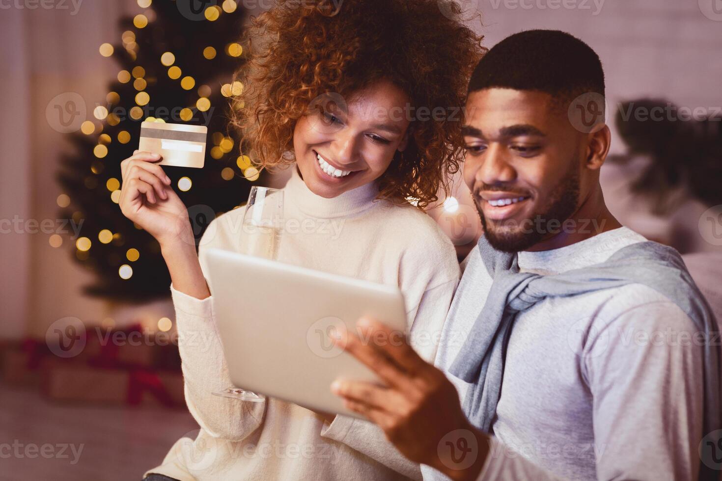 Christmas preparation. Happy black couple buying gifts online, using tablet and credit card photo