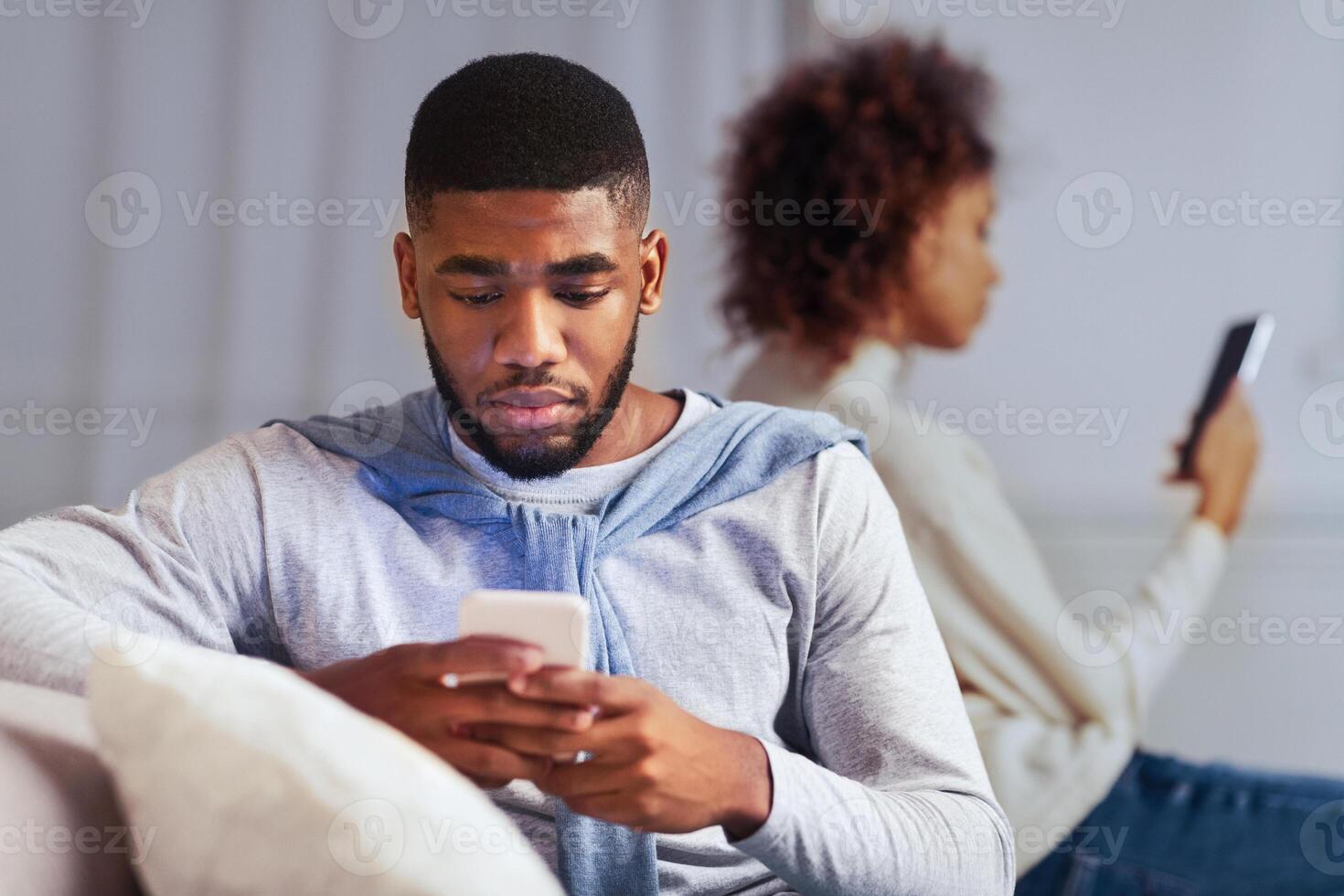 Indifference in relationships. Black couple using cellphones and ignoring one another photo