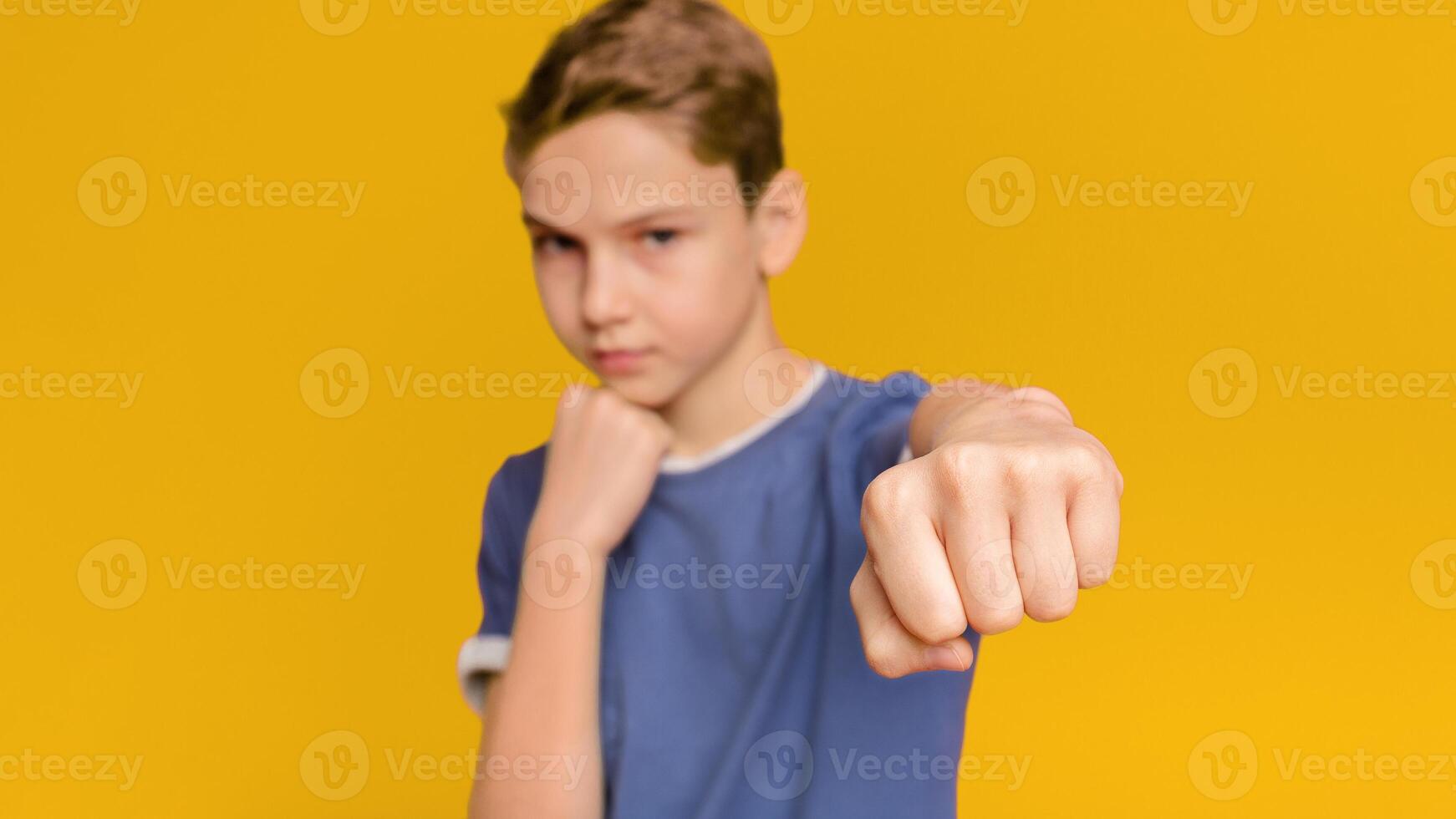 Serious teen boy training box punch, focus on fist, orange studio background photo