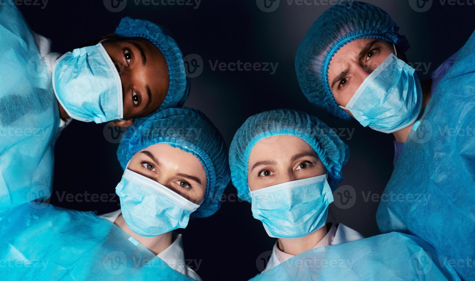 Patient pov. Team of surgeons looking at patient after performing operation in dark room photo