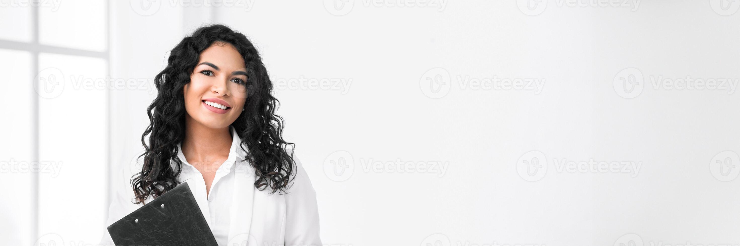 Successful Businesswoman. Portrait of smiling hispanic manager standing with clipboard, looking at camera, free space photo