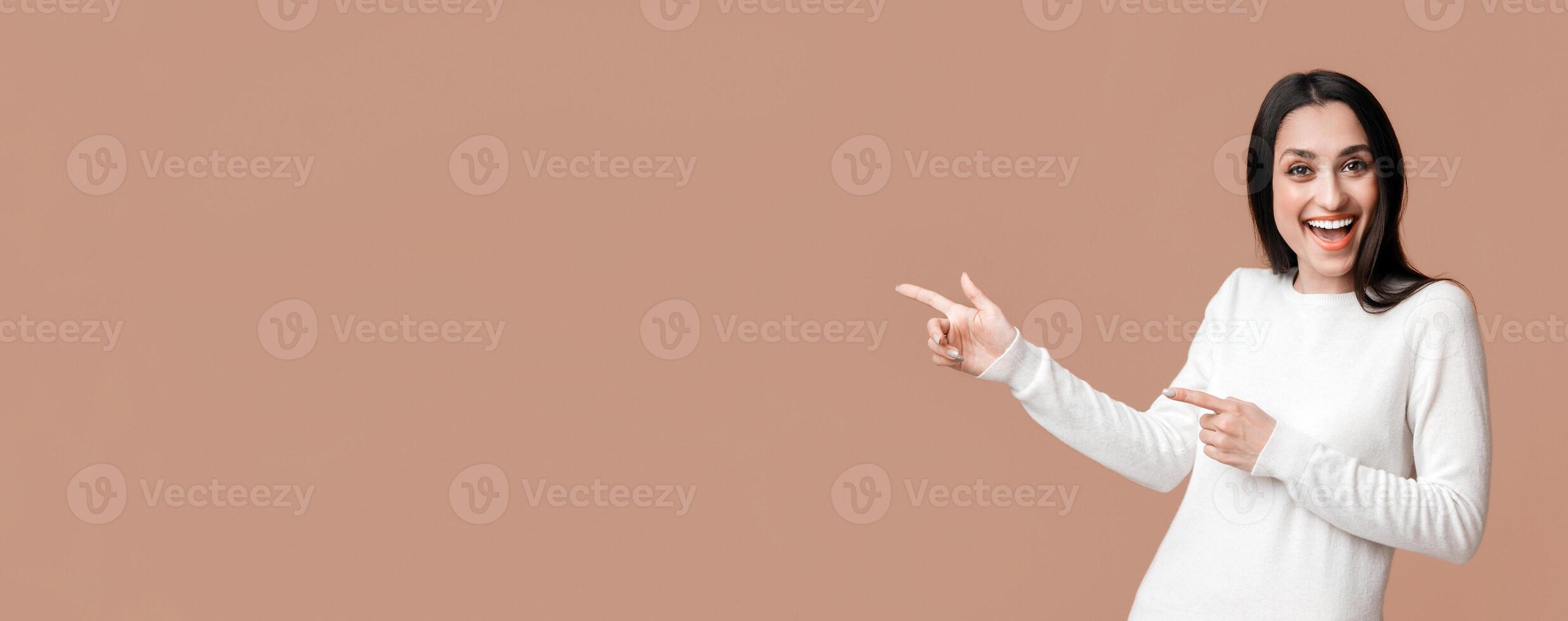 Cool offer. Joyful brunette girl pointing at copy space over yellow background with two hands, recommending something, panorama with empty space photo