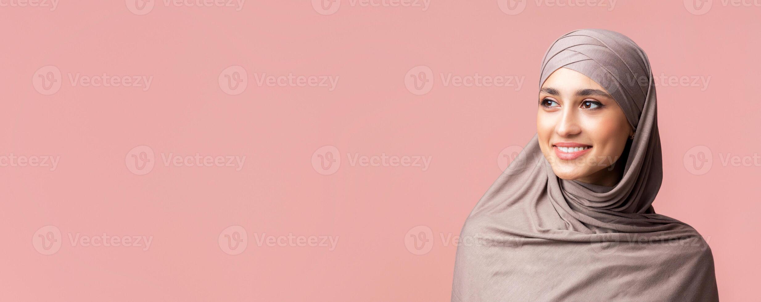 Millennial muslim woman. Portrait of attractive islamic girl in hijab looking away over pink background with copy space, closeup photo