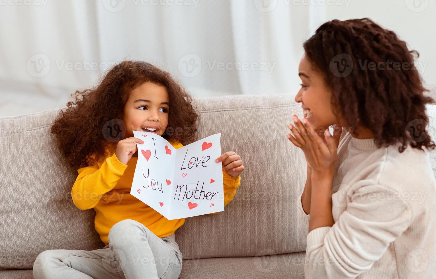 Mother's Day. Little Daughter Congratulating Mother On Holiday Or Birthday Giving Self-Made Postcard Sitting Together On Sofa At Home. photo
