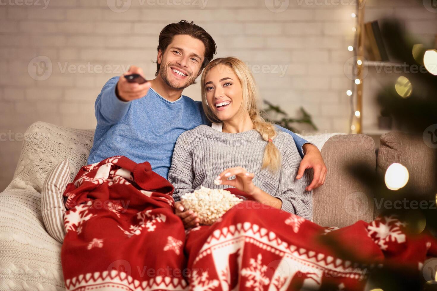 Christmas eve. Loving couple watching tv and eating popcorn at home, covered with blanket photo