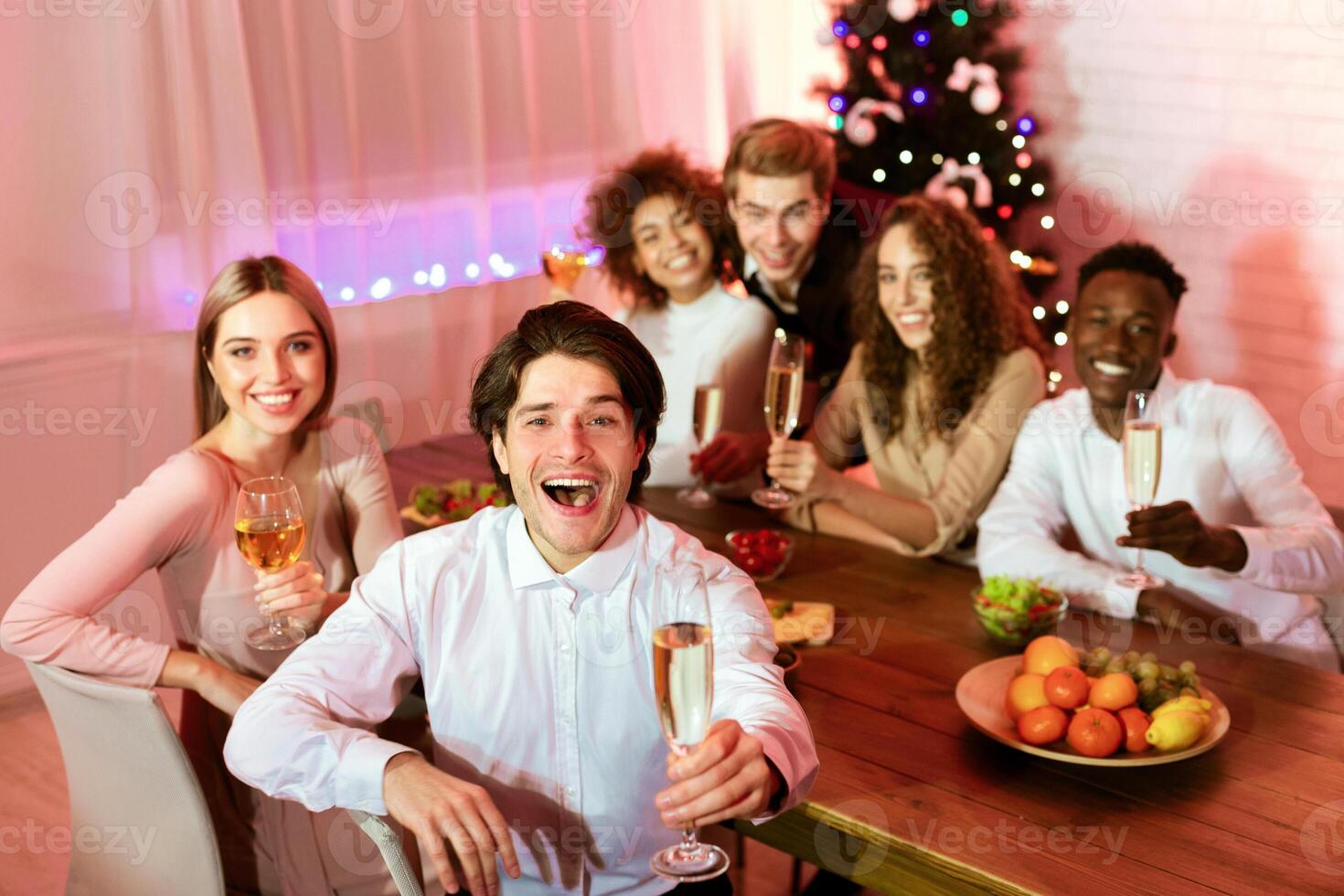 Cheers. Happy Group Of Millennial Friends Holding Glasses Smiling At Camera Sitting At Table Having Christmas Home Party Indoor photo