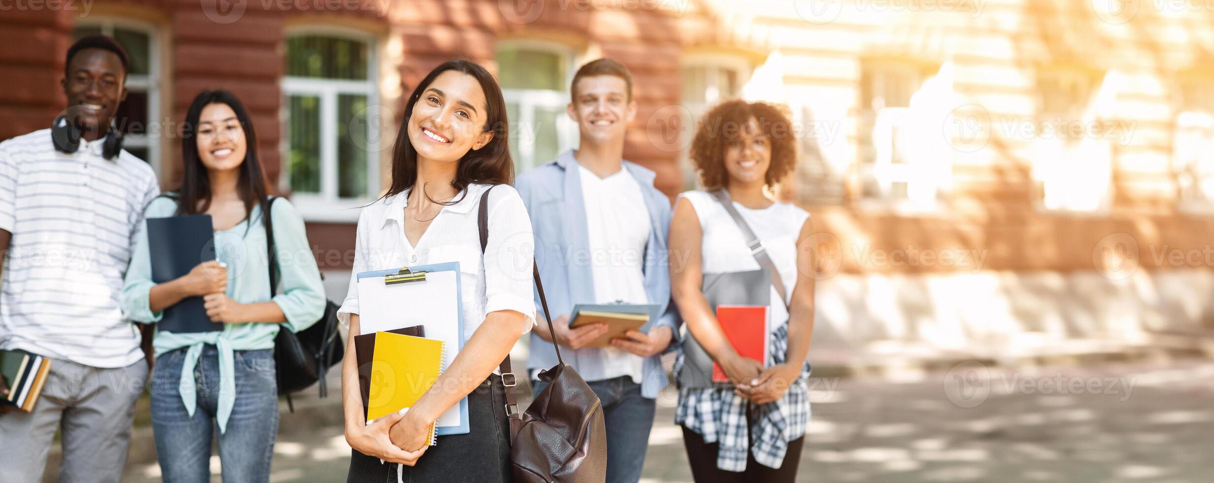 Future Professionals. Portrait of diverse university students posing outdoors in campus, selective focus on arabic girl with notepads photo
