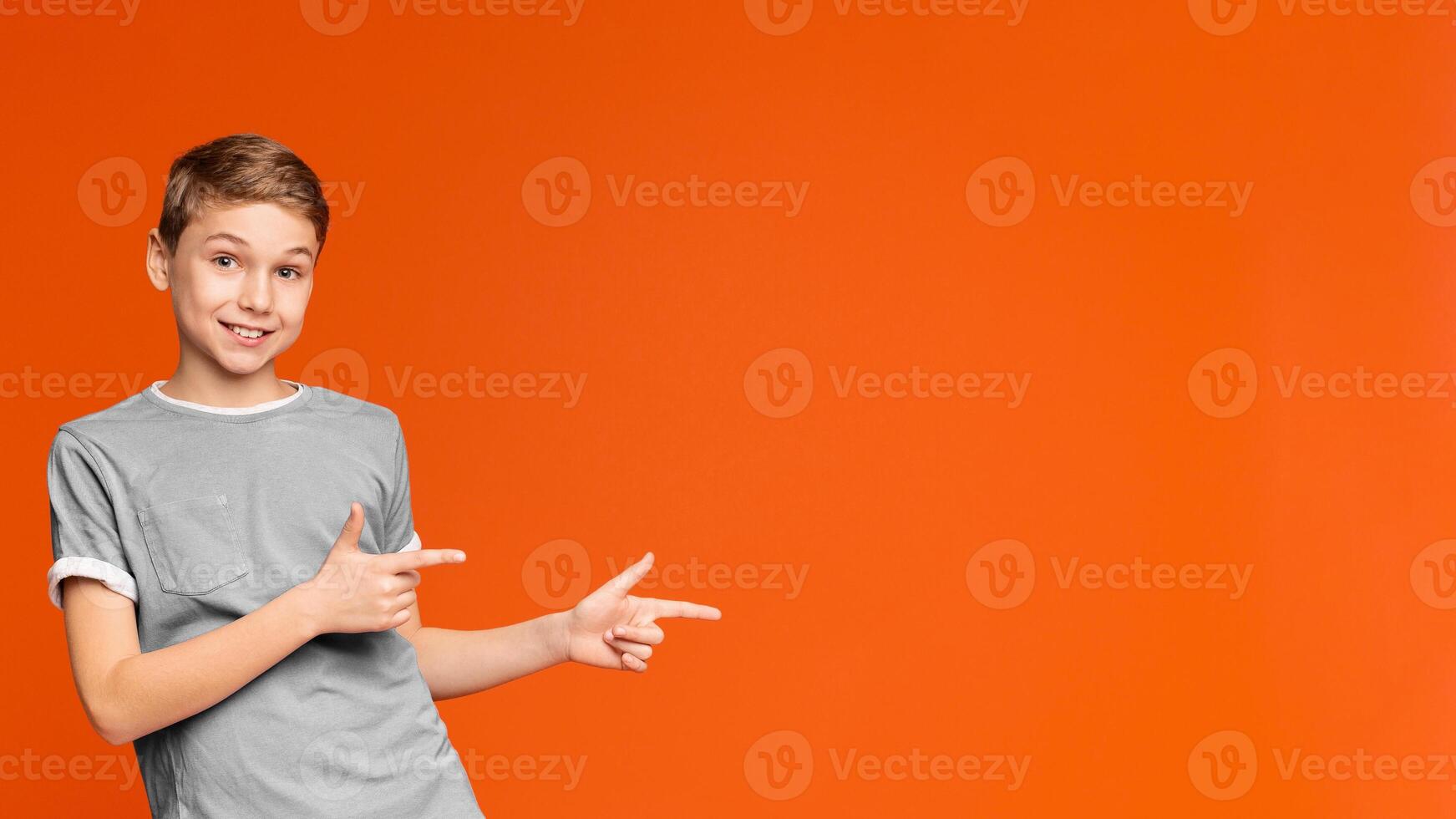 Cute little boy pointing away at empty space on orange studio background photo