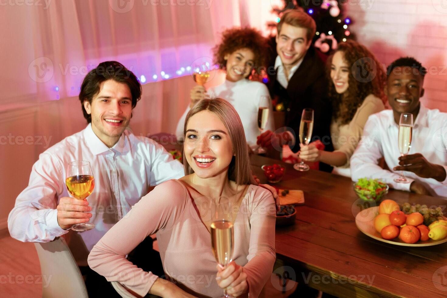 Happy New Year. Young People Having Xmas Dinner Holding Champagne Glasses Smiling At Camera Celebrating At Table At Home photo