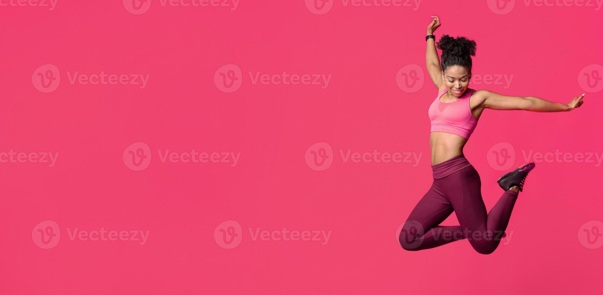 Happy athletic black girl in sportwear jumping up over red background, healthy lifestyle concept photo
