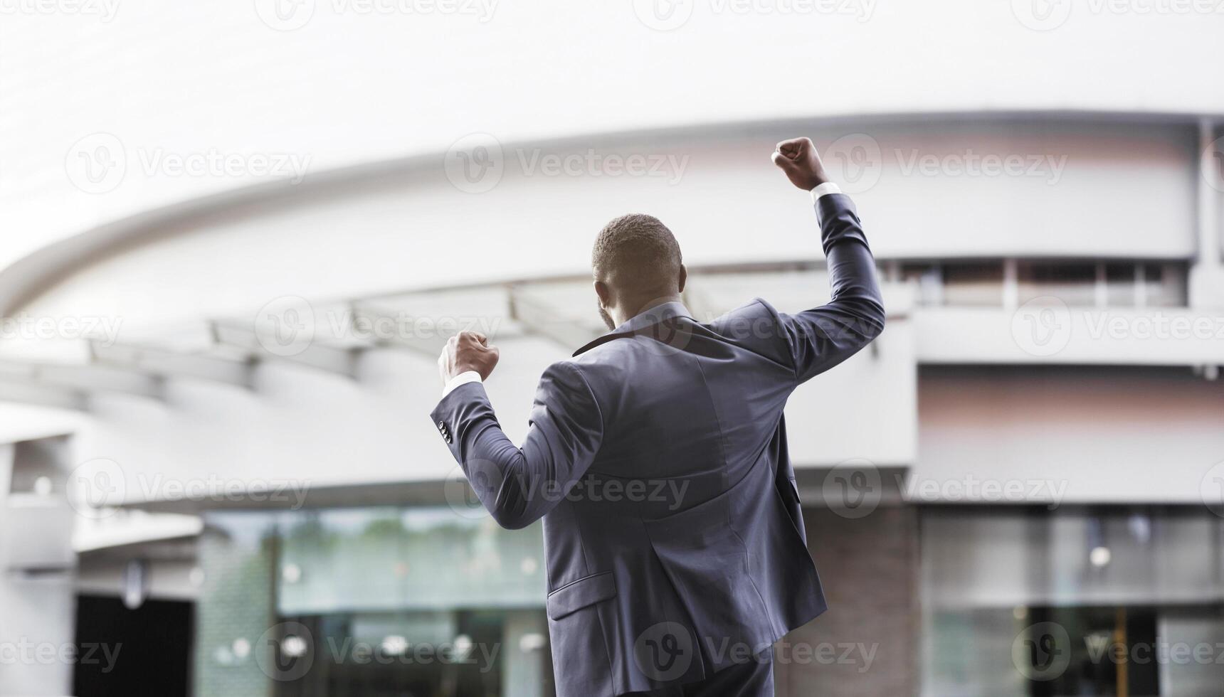 African american job seeker celebrating successful interview raising fists against business center, rear view with copy space photo
