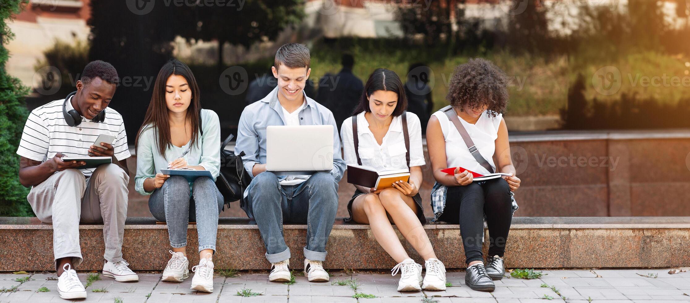 Preparing For Lectures. Group Of Multi-Ethnic Students Studying Together Outdoors, Using Laptop And Taking Notes To Workbooks, Panorama photo