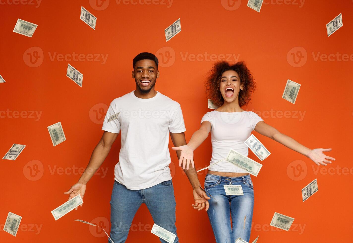 Lottery winning. Emotional rich african-american couple enjoying money banknotes shower, orange background photo