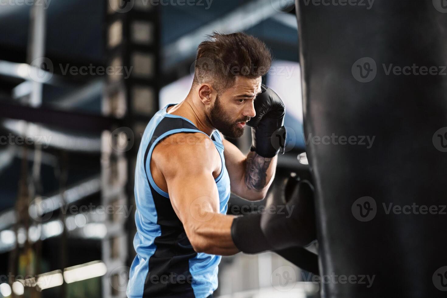 Boxing training. Active guy punching boxing bag at gym, empty space photo
