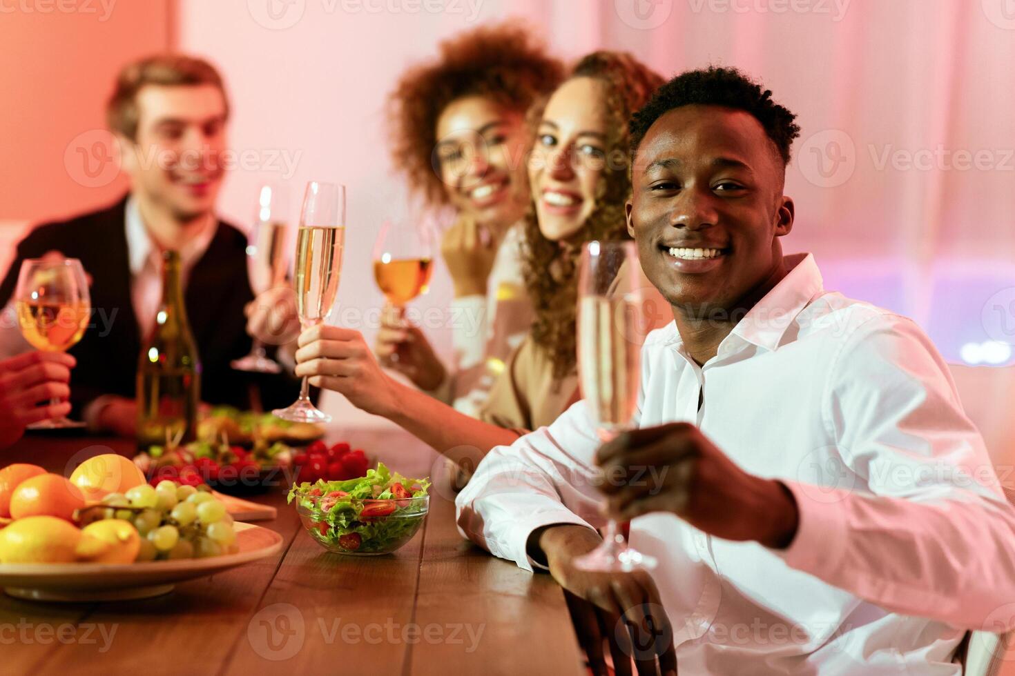 Happy New Year. Joyful Multiethnic Friends Celebrating Christmas Holiday Drinking Champagne Smiling To Camera During Dinner At Home. Selective Focus photo