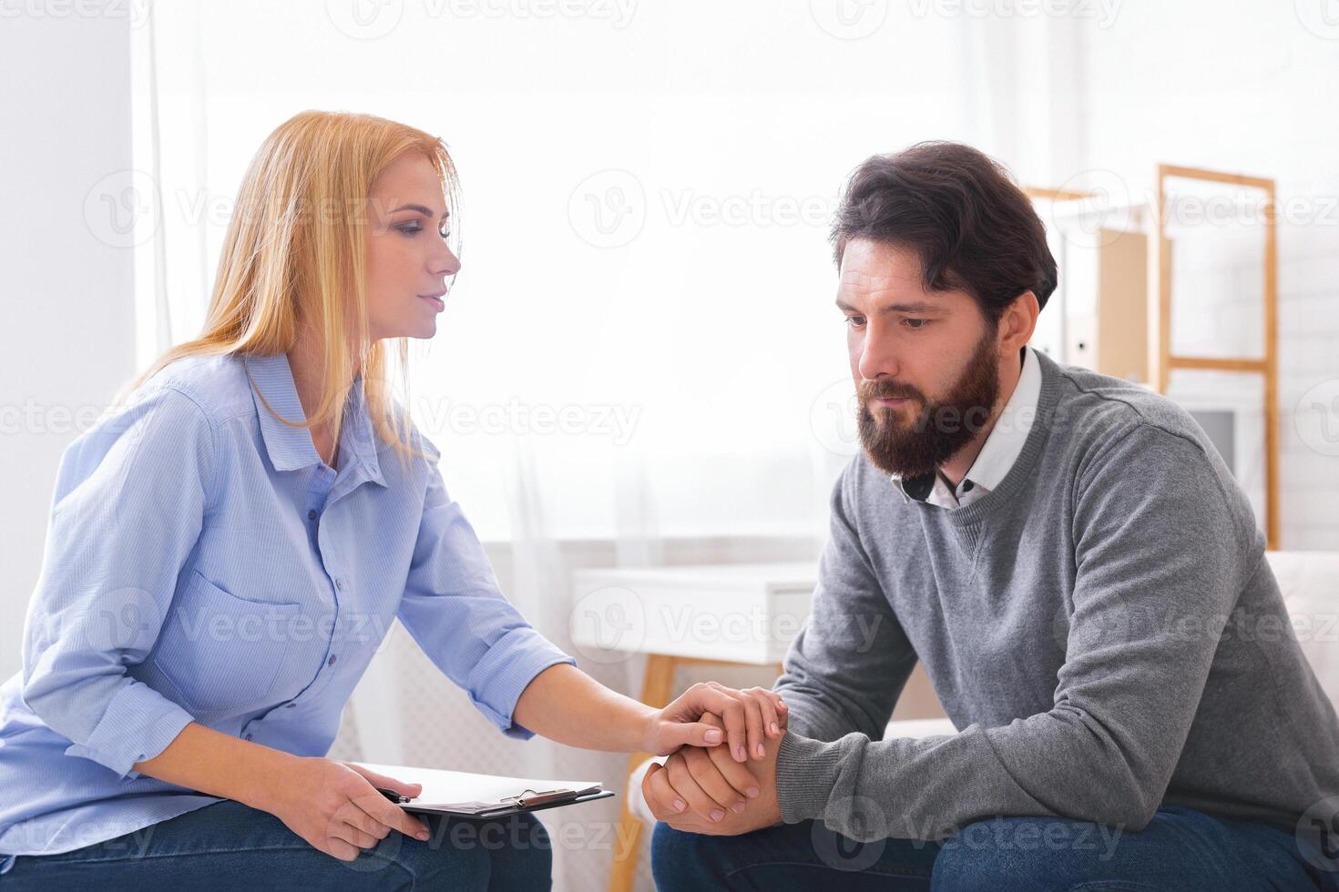 A man sitting down appears to be sharing personal concerns with a woman, possibly a counselor or therapist, who is attentively listening and taking notes. photo