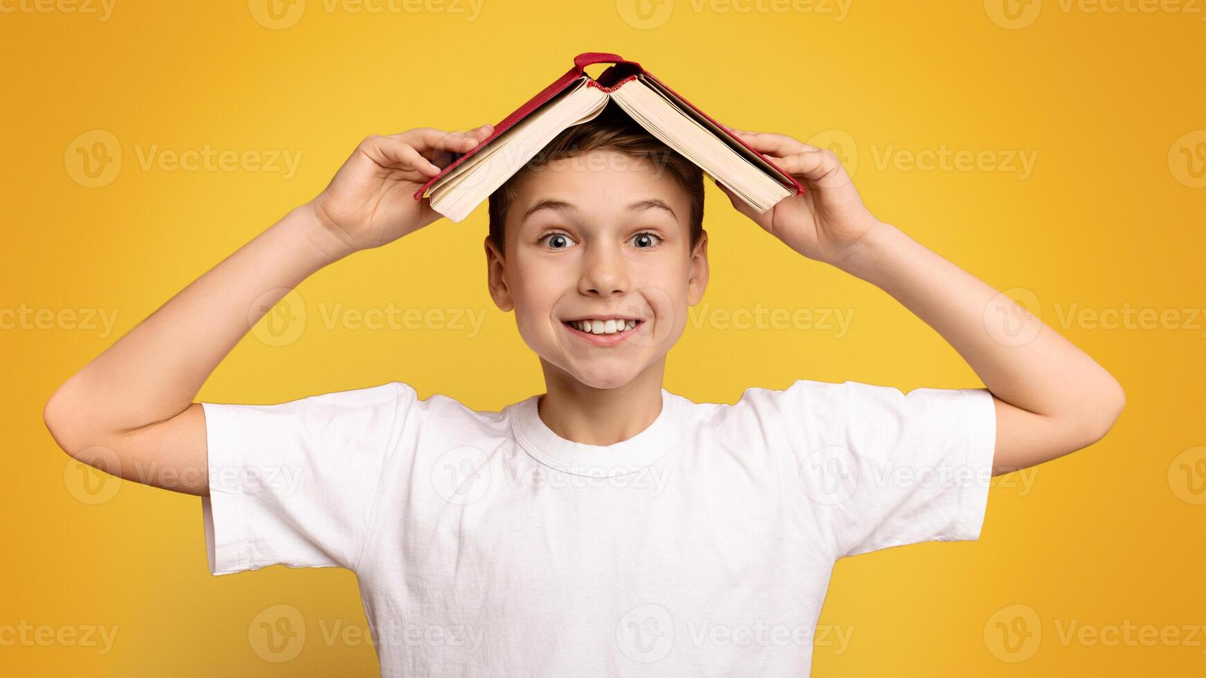 A young boy stands with a book raised above his head. photo