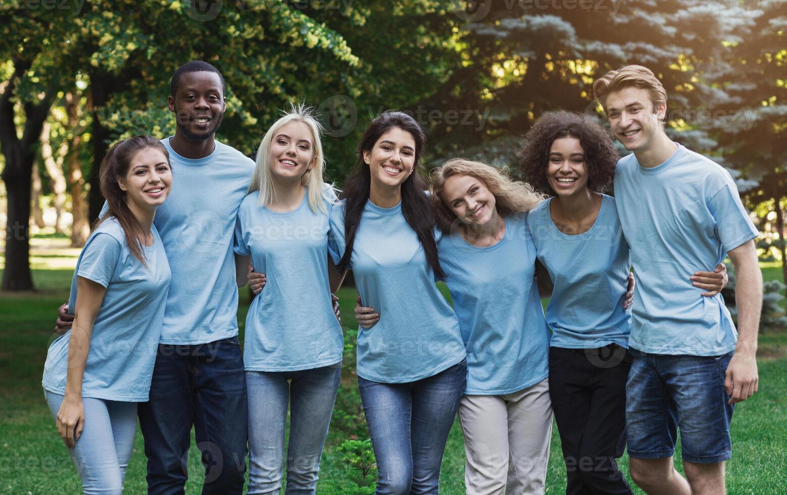Group of happy young diverse volunteers embracing at park, ready for work, copy space photo