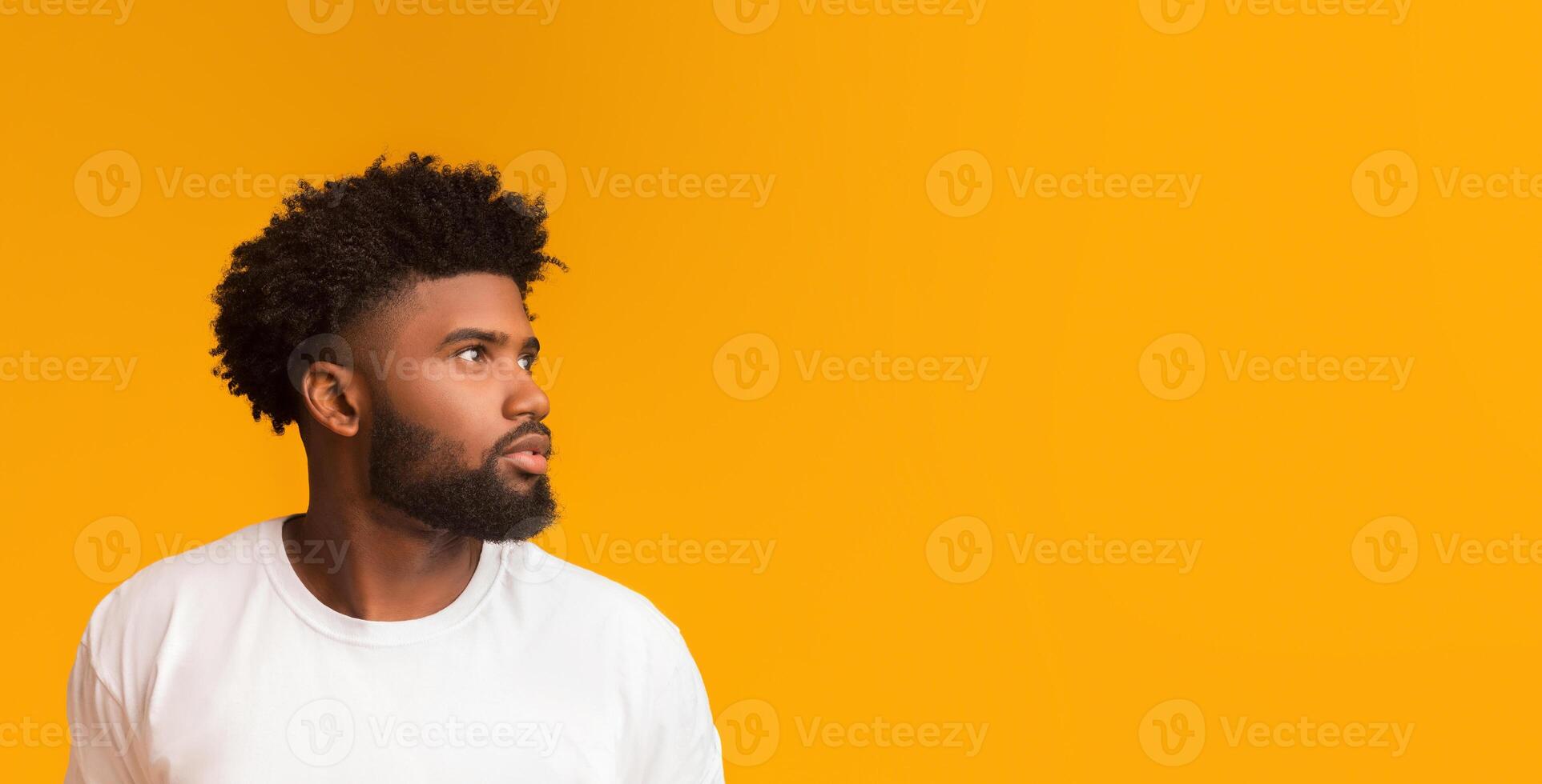 Skeptical young african american man looking aside at free space on orange background photo