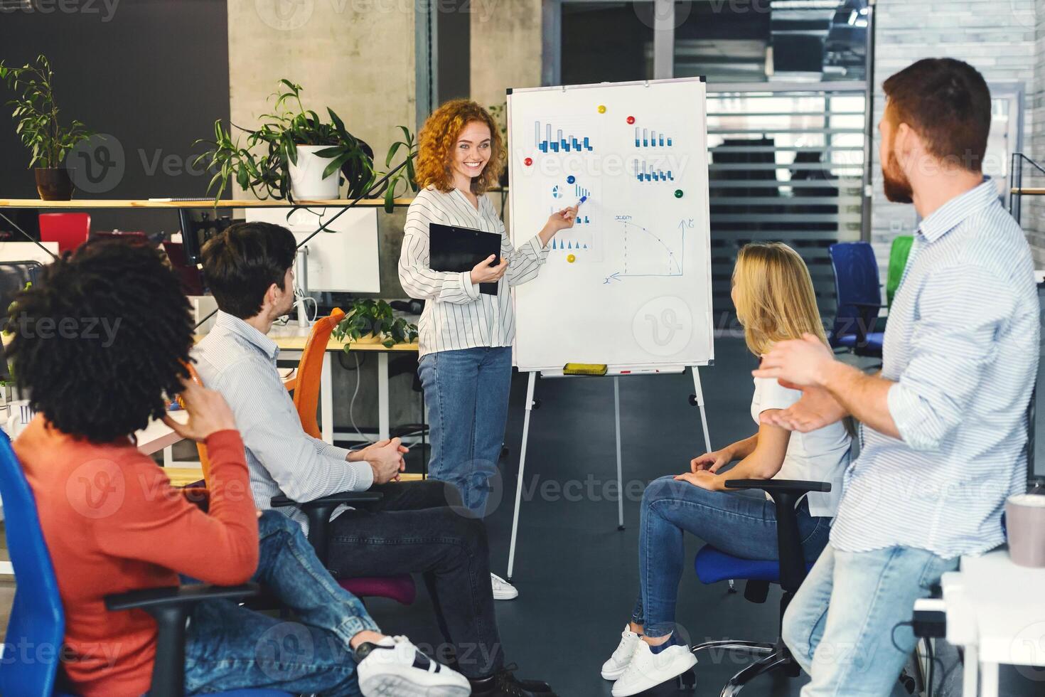 A group of diverse individuals sitting around a whiteboard in a meeting room, discussing and brainstorming ideas. Some are writing notes, others are listening attentively. photo
