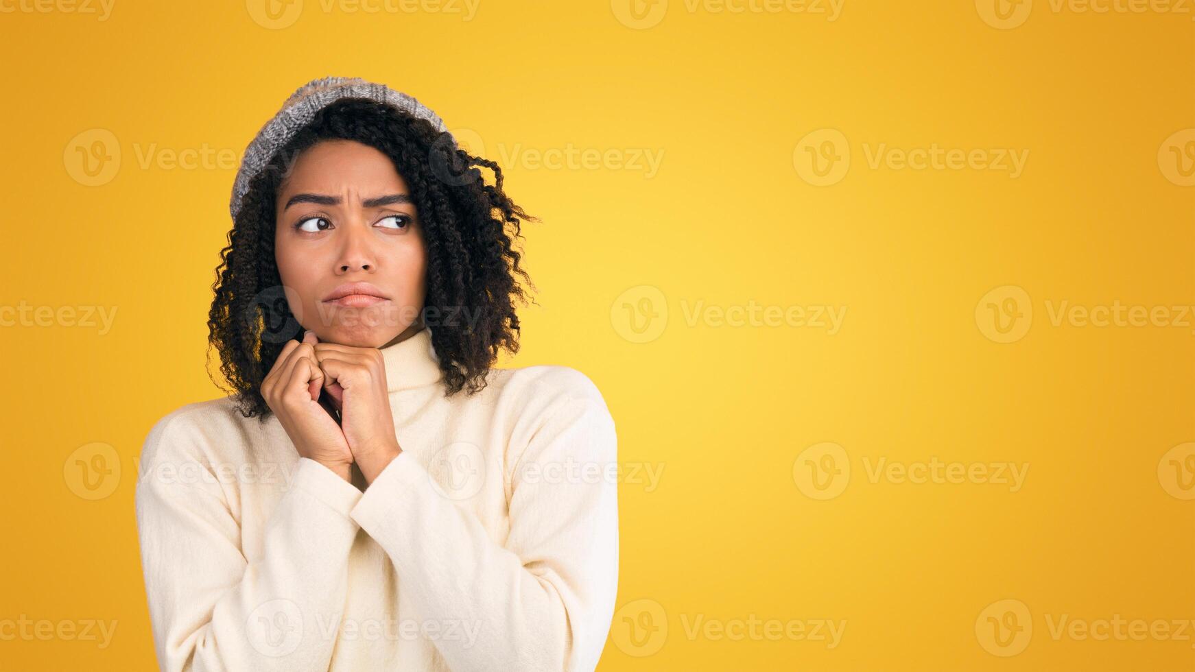Cold Home. Upset african american girl in wool hat freezing, trying to warm up isolated over yellow studio background photo