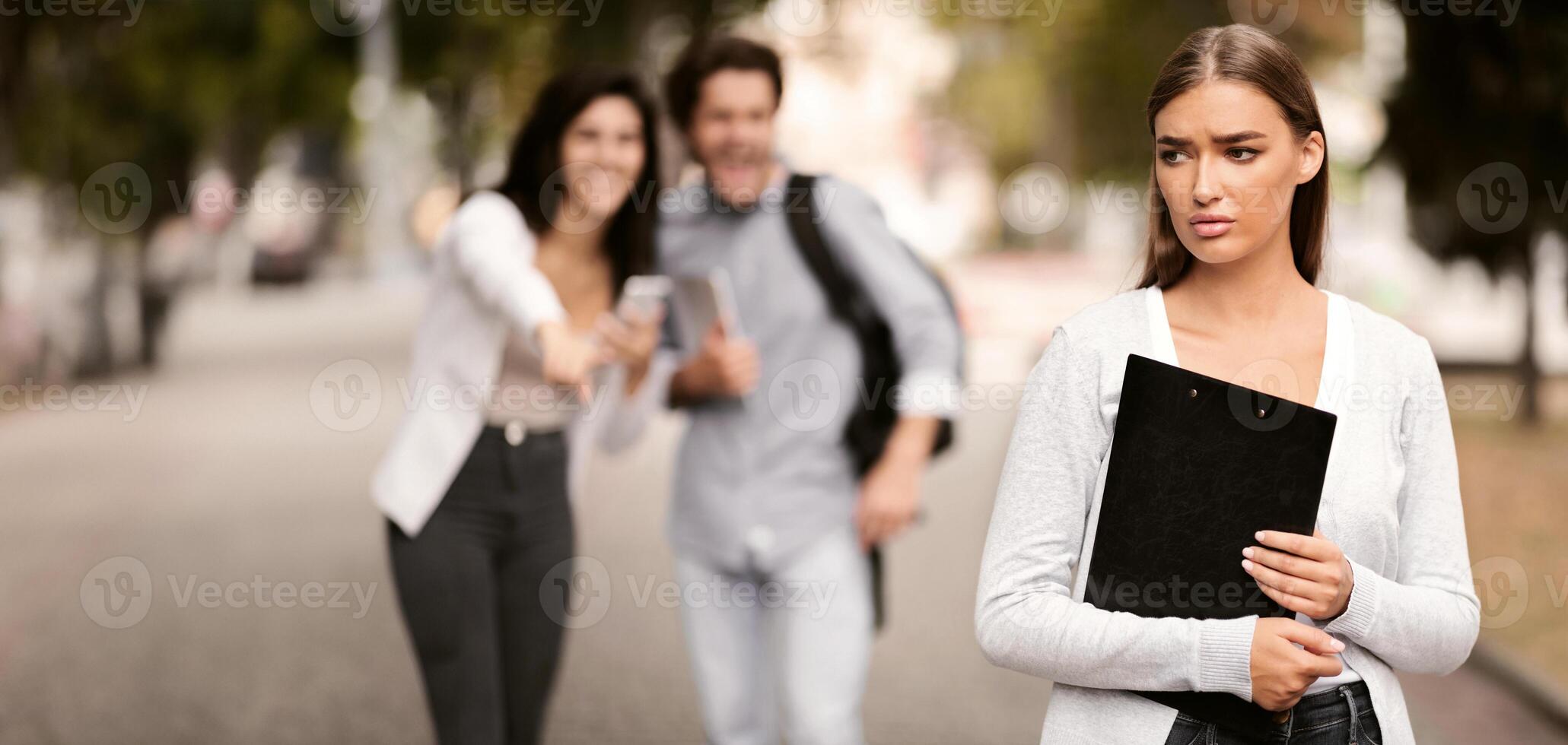 Bullying Concept. Unhappy Girl Being Bullied By Couple Of Students Walking Outdoor. Selective Focus. photo