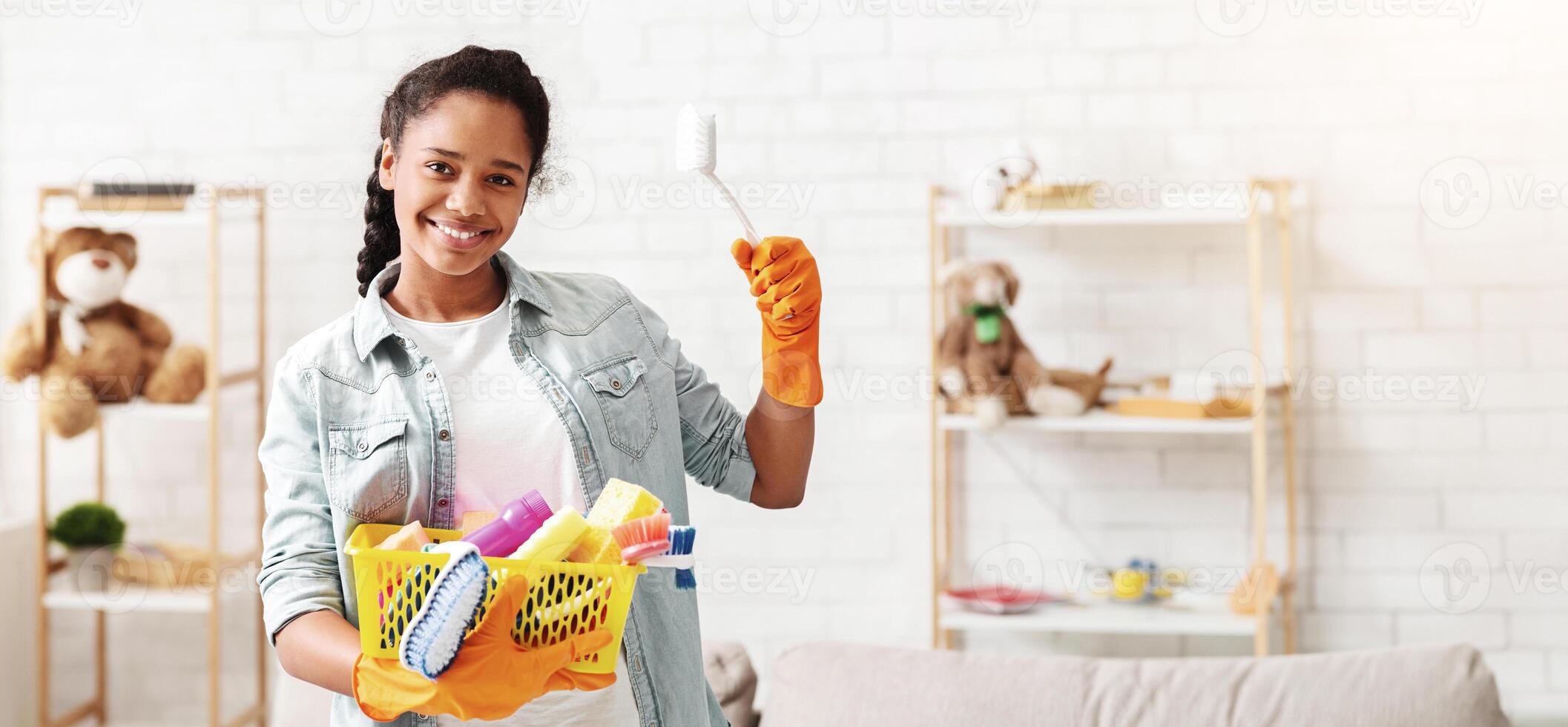 Cheerful tidy african american teen girl holding cleaning tools, going to clean her room, empty space photo