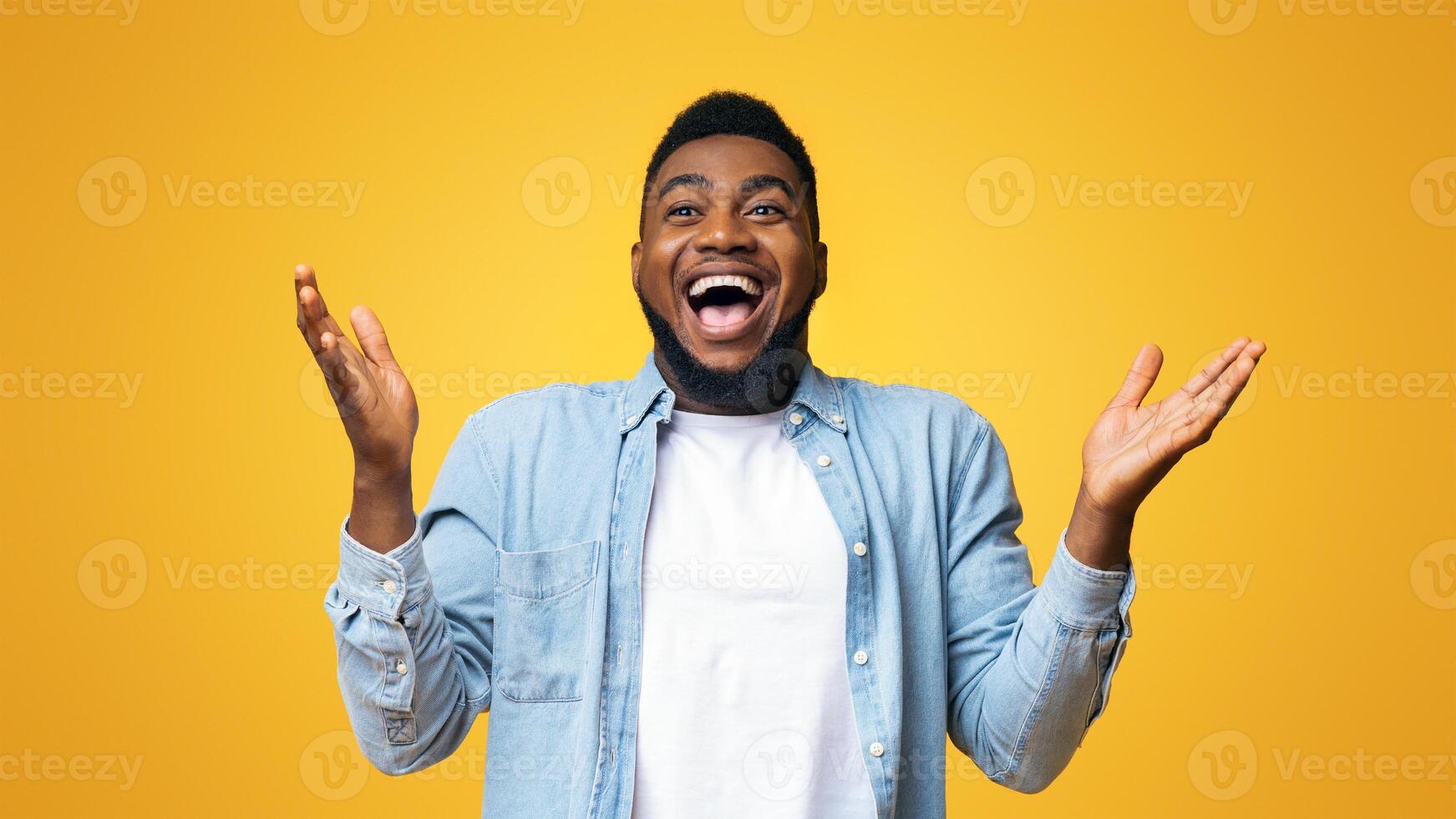 I can not believe. Portrait of joyful african american man raising hands in the air with excitement and looking at camera, yellow studio background. photo