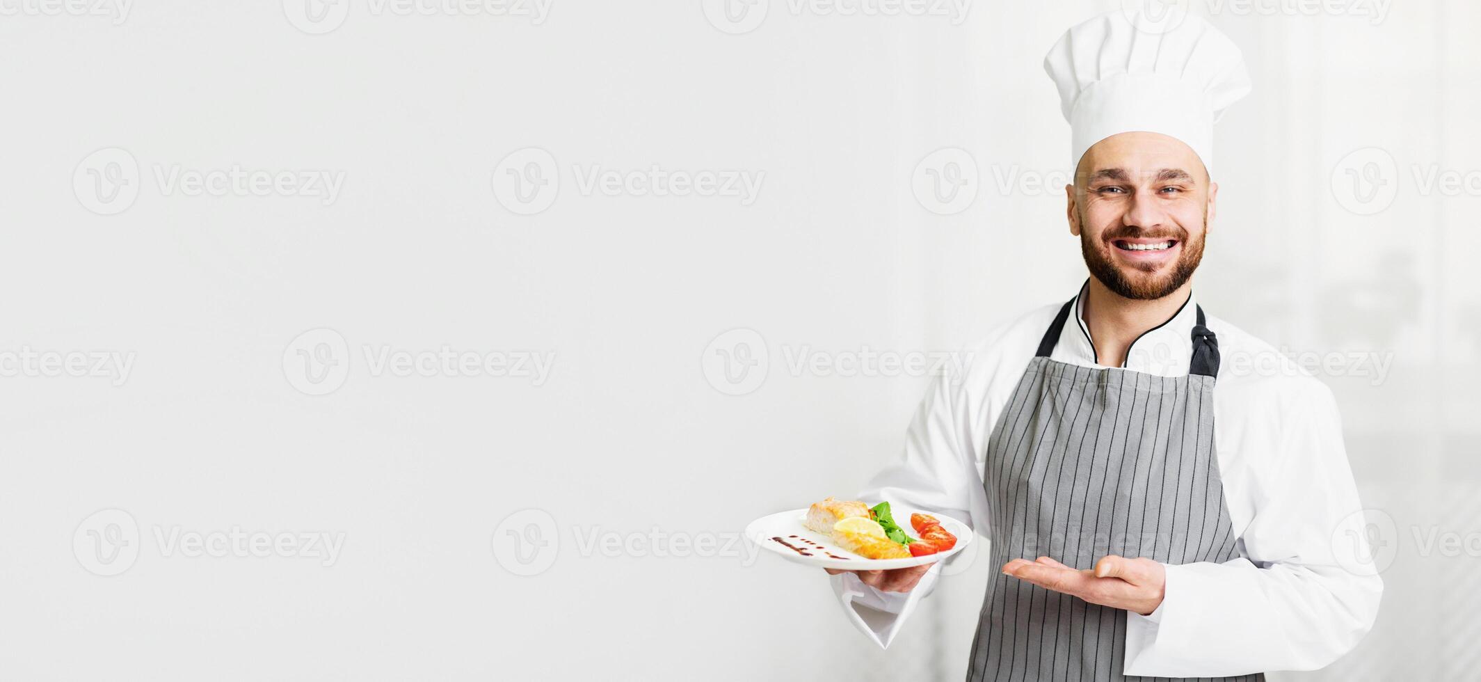Fish Recipes. Cheerful Chef Man Holding Plate With Roasted Salmon Steak Serving Dish Standing In Kitchen. Selective Focus photo