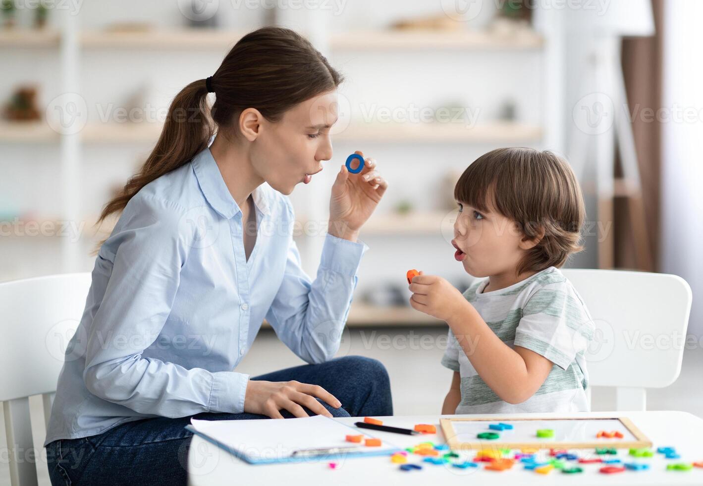 Female speech therapist curing child's problems and impediments. Little boy learning letter O with private English language tutor during lesson at office photo