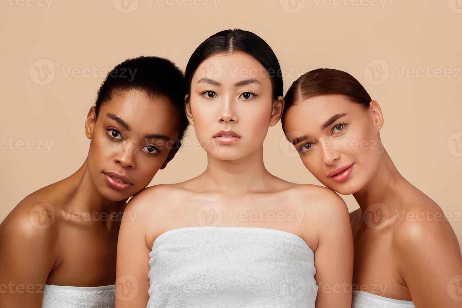 Body Care. Three Sensual Women Wrapped In White Bath Towels Posing Over Gray Background, Looking At Camera. Studio Shot photo