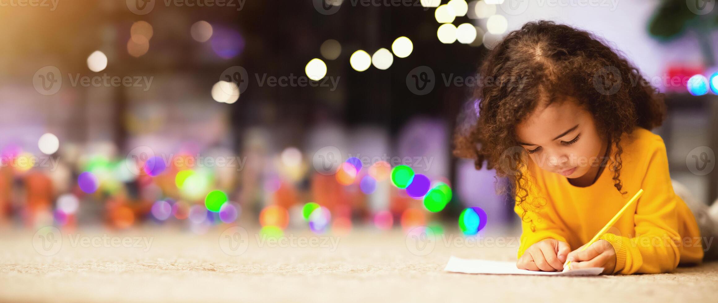Christmas art. Little black girl drawing on floor near xmas tree, empty space photo