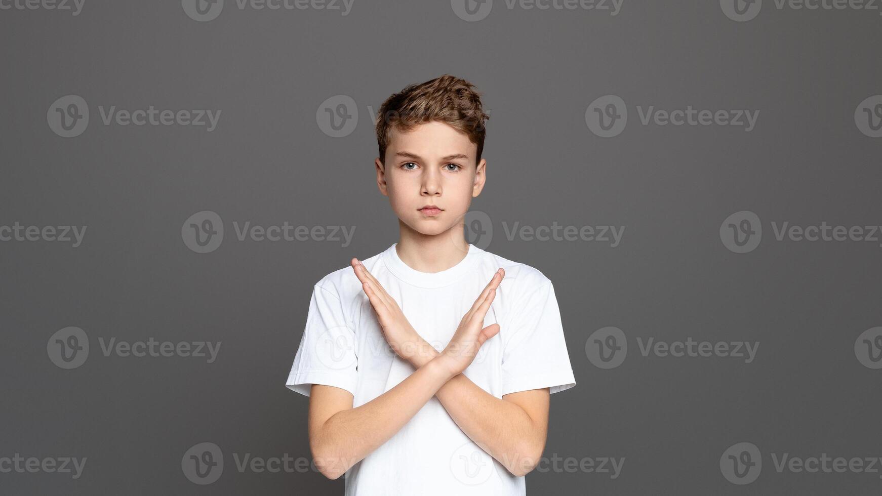 Teenager with arms crossed in an X shape, showcasing refusal or denial, isolated on a grey background photo