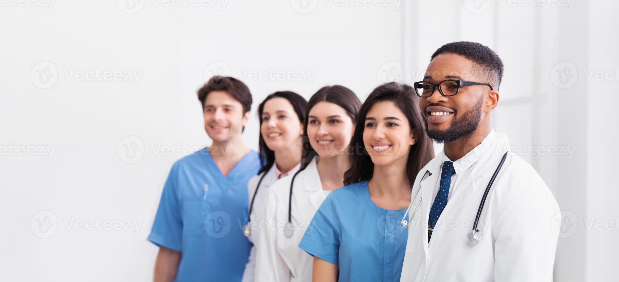 Team of doctors and interns standing in hospital in row and looking aside photo