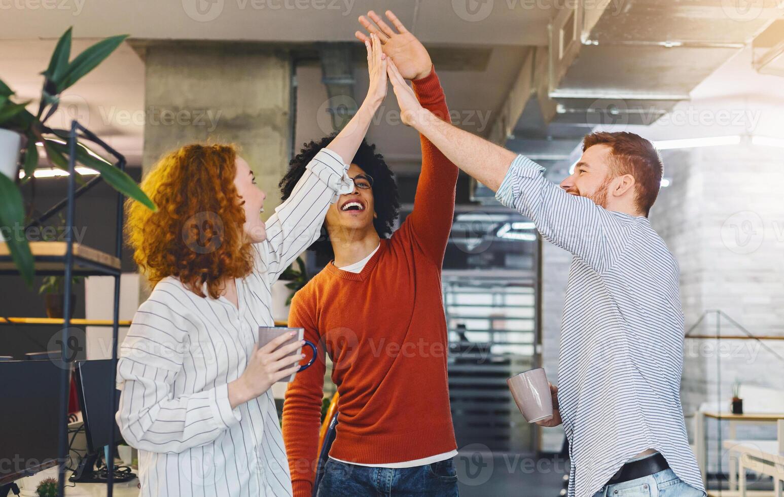 Happy coworkers having fun, giving high five during friendly talk in office, coffee break. photo