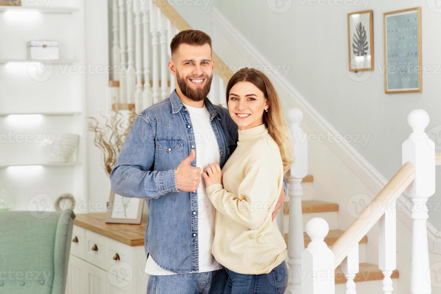 A man and woman are standing side by side in front of a staircase, looking towards the camera. photo