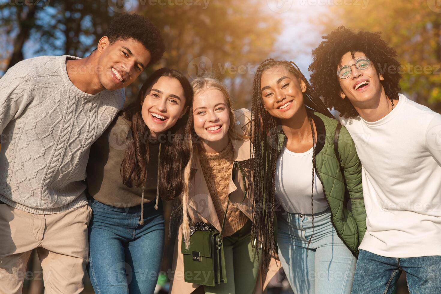 Group portrait of happy multiracial teenaged friends spending time together in autumn park photo