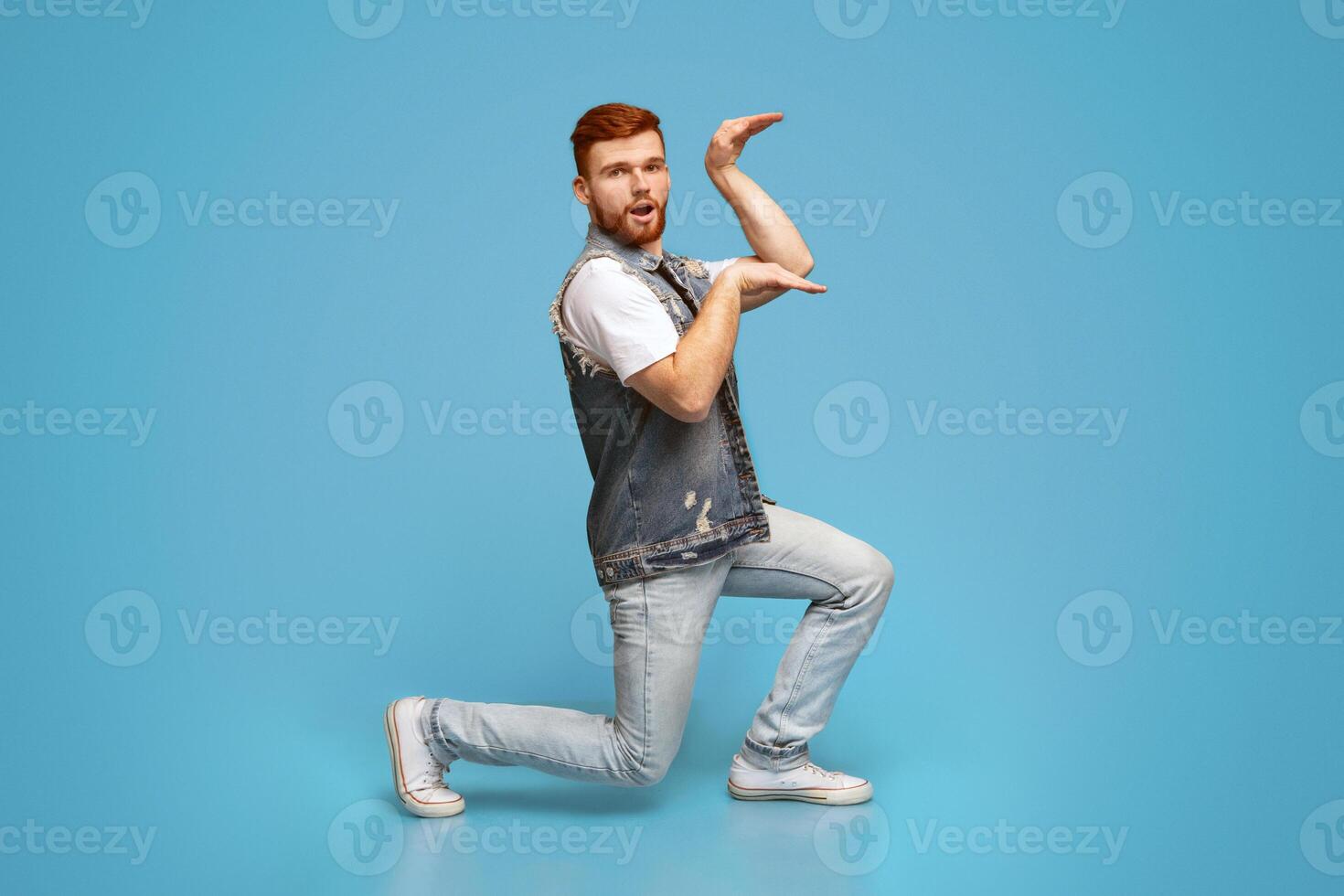 Funny millennial guy dancing in Egyptian style posing isolated on blue background, studio, copy space photo