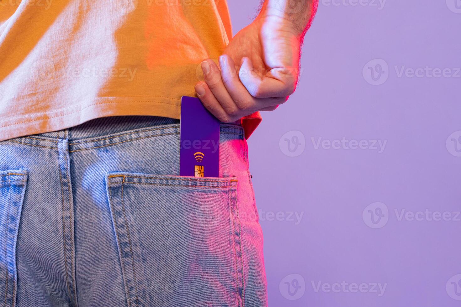 Cropped of man is shown holding a purple card and placing it inside their pocket. The individuals hand is clearly visible as they perform this action. photo