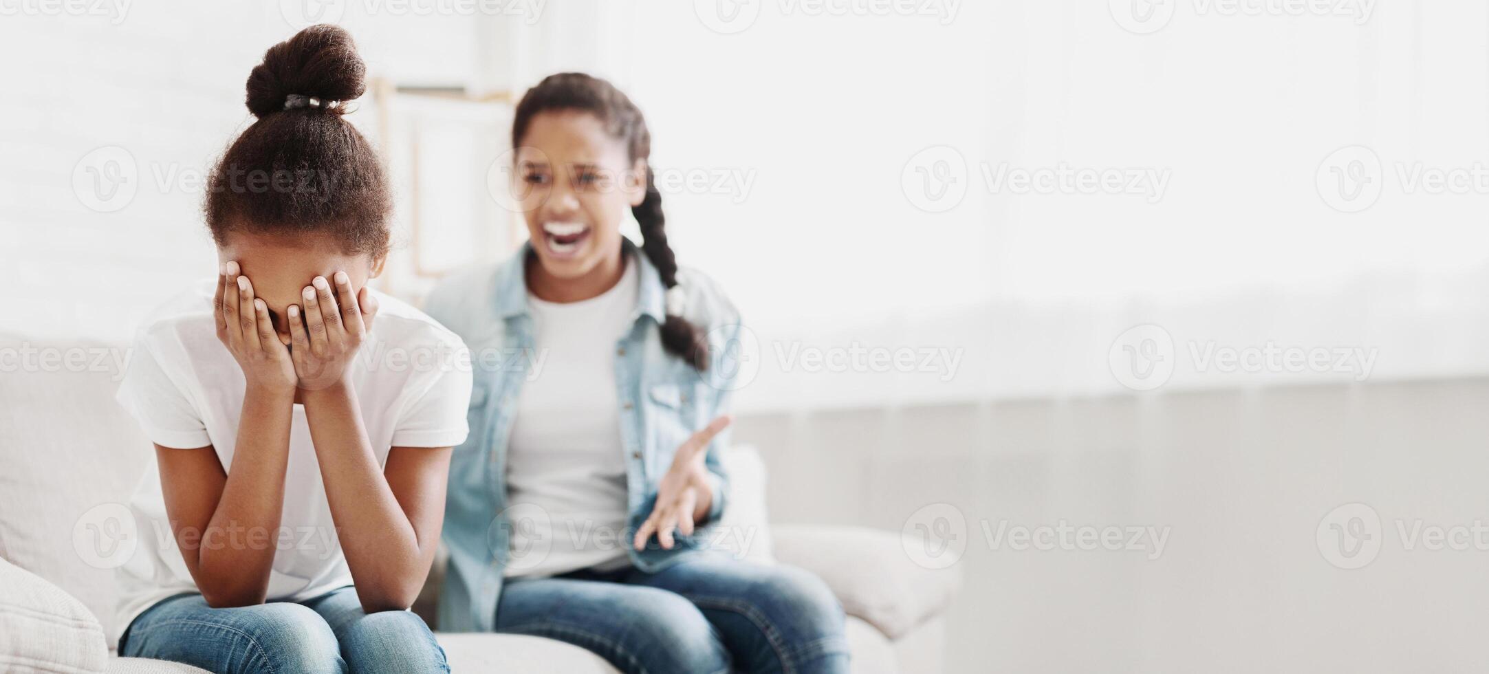 Generation conflict. Furious african girl yelling at her sister, little girl closing her eyes, home interior, copy space photo