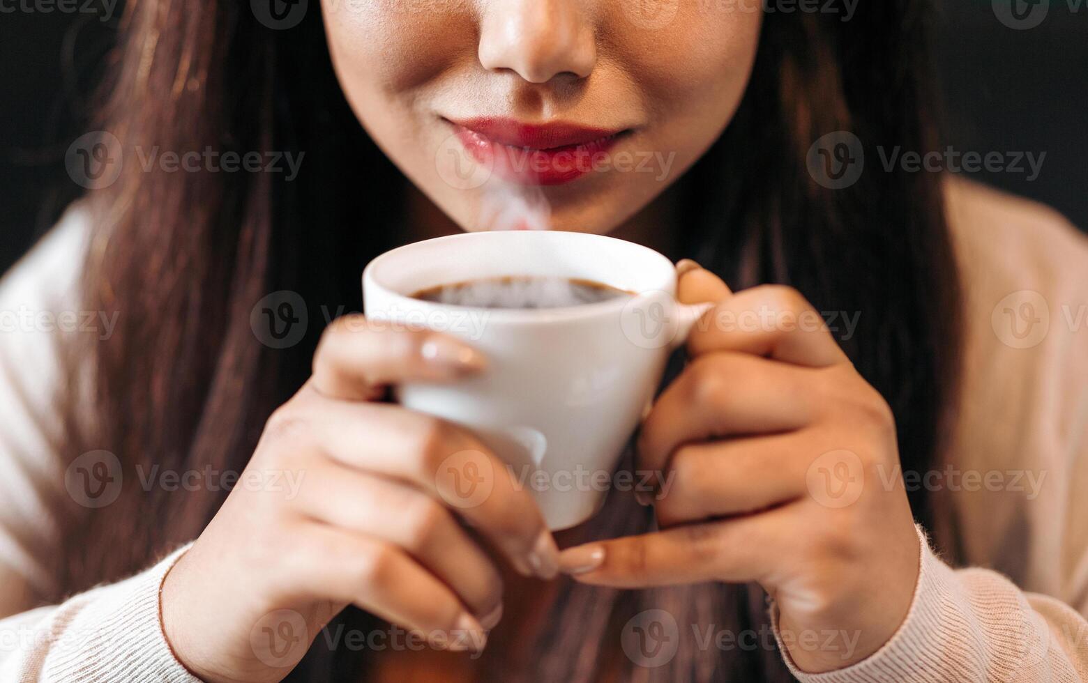 Cropped of girl is holding a cup of coffee in her hand, with steam rising from the hot beverage, enjoying a moment of relaxation and warmth while savoring the aroma and taste of the coffee. photo