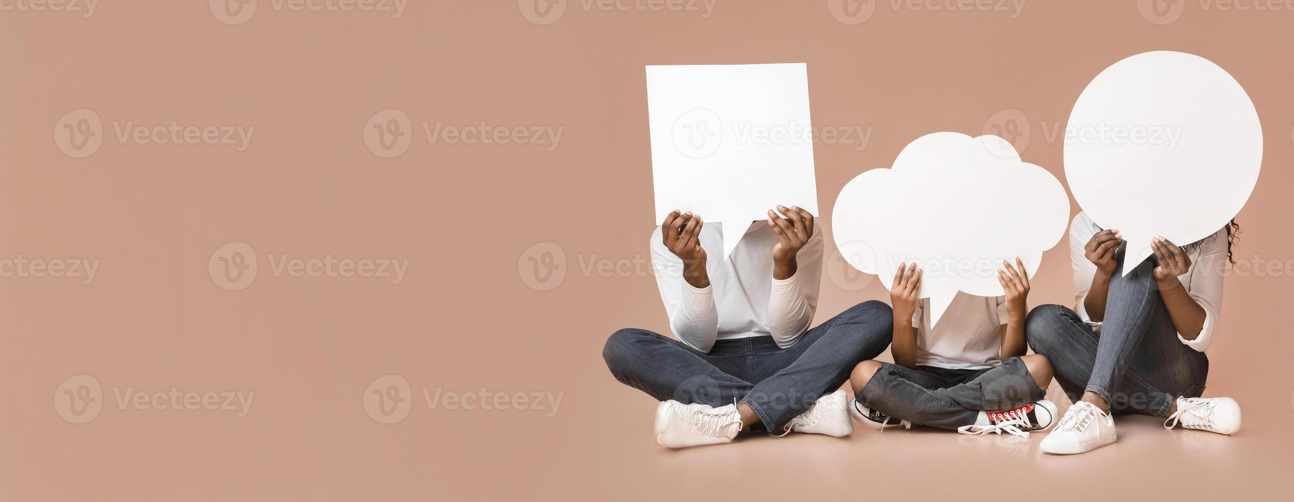 Diverse thoughts. Black family of three holding empty speech bubbles in front of their heads, sitting on floor over yellow background. photo