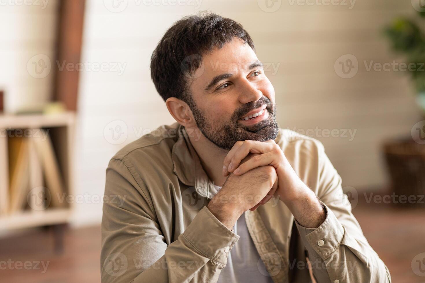 A man is seated at a table, his hands folded neatly in front of him. He appears deep in thought, with a focused expression on his face. photo