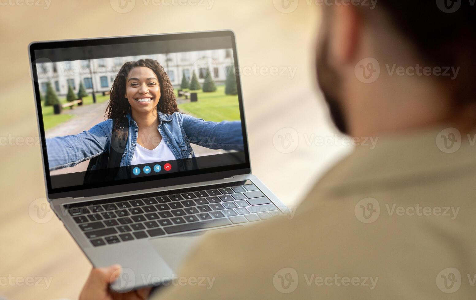 African American woman is on a call with someone on a laptop computer. She is smiling and waving, and appears to be in a park setting. She is likely calling a friend photo